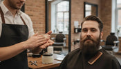Barber warming beard balm between his palms beside a client with a full beard