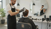 A barber applying light hair mousse foam to a client's hair for volume and curl definition in a modern barbershop