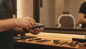 Professional barber adjusting clipper blades at a wooden barber station in a warm barbershop environment