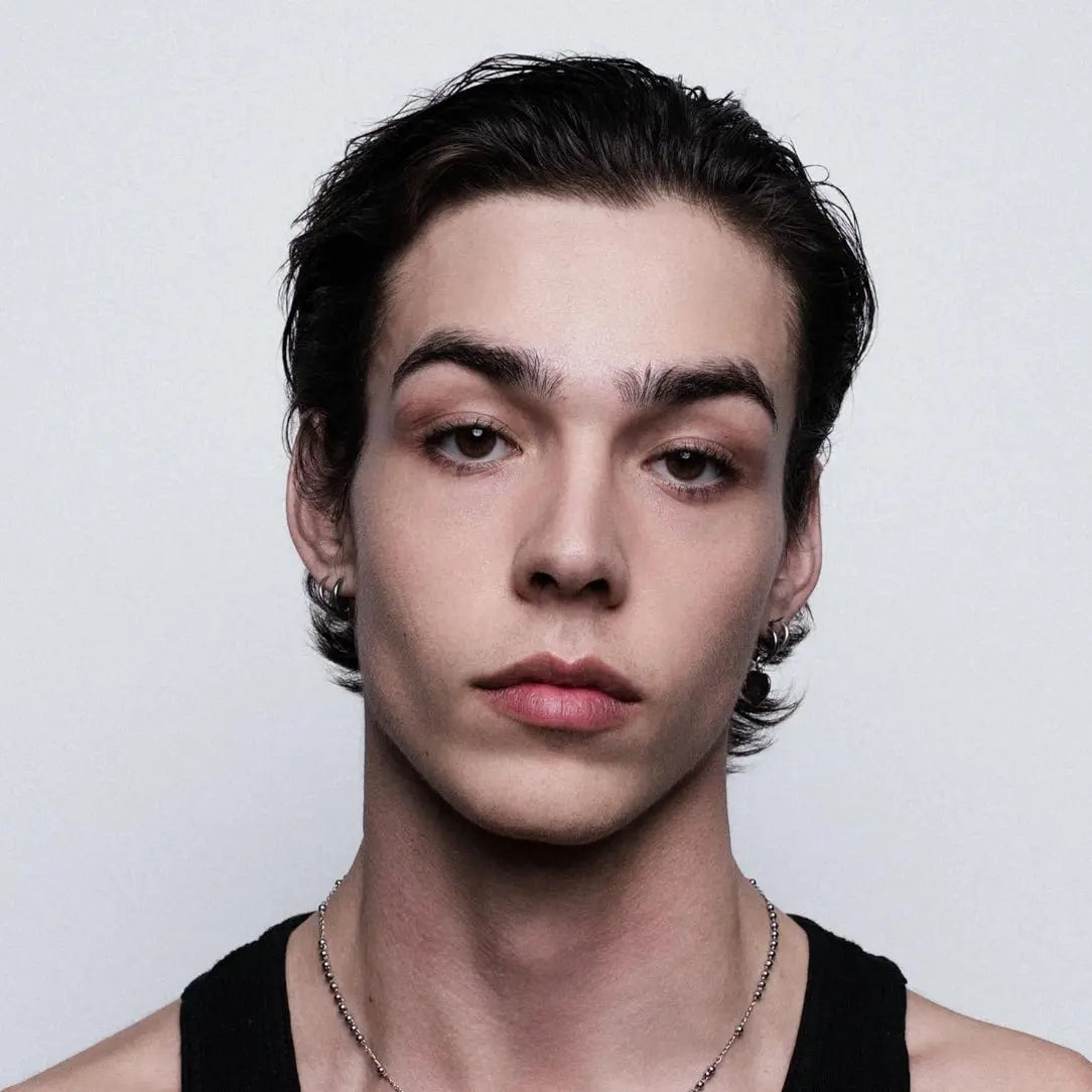 Person with styled hair and a black tank top against a plain background