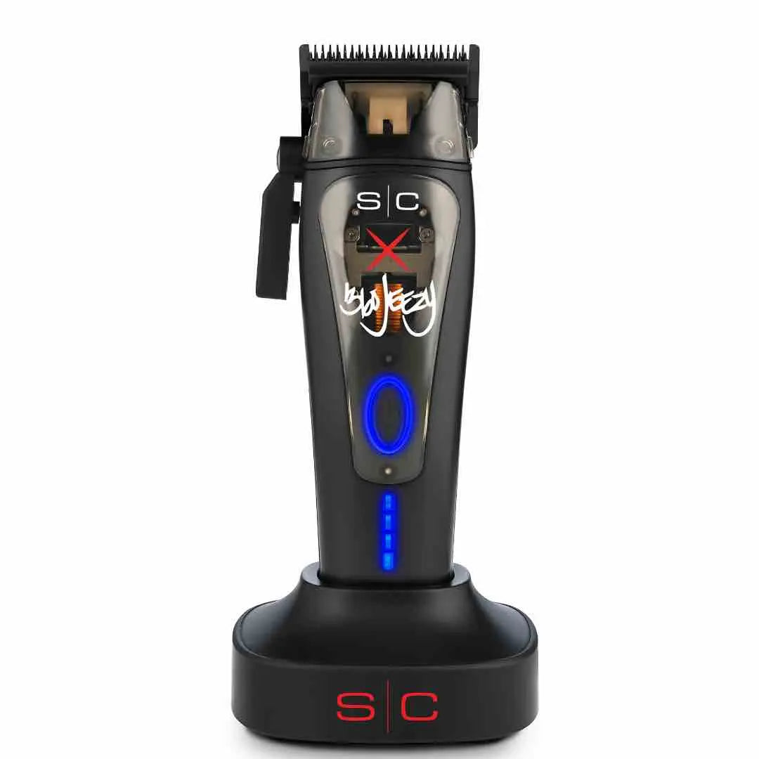 A professional cordless hair clipper with a black body, blue light indicators, and a charging stand. The clipper has a signature on the blade and branding elements.