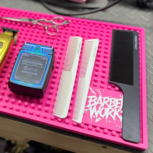 "Barber Works Professional Station Mat with combs, clippers, and scissors on a vibrant pink mat, showcasing barber tools."