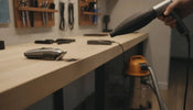 Cordless air blower clearing hair clippings from a powered-off clipper on a barber workbench
