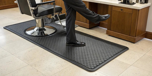 Thick anti-fatigue barber mat at a salon station for all-day comfort and posture support.