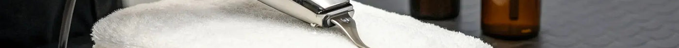 Barber maintaining professional clippers with oil, brushes, and cleaning spray on a workstation.