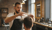 Barber working hair styling powder into a client's roots to build volume in a barbershop
