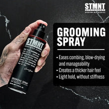 Hand holding a STMNT  grooming spray bottle with product details on a black background