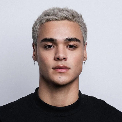 Person with short, styled hair wearing a black shirt against a plain background