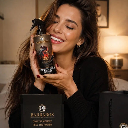 A woman in a black sweater holds a bottle of Barbaros Captain Cool Hair Spray next to a black branded gift box in a warmly lit indoor setting.