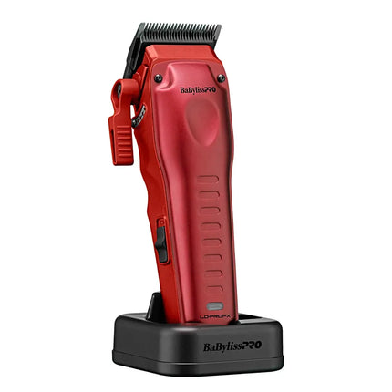A red BaBylissPRO cordless hair clipper standing upright on a black charging dock against a plain white background.
