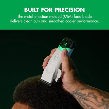 A close-up of a tattooed hand holding a white and black BaBylissPRO Tomb45 White Wireless against a dark background, clipping hair on a person's head. A green banner at the top reads 'BUILT FOR PRECISION' with descriptive text about the metal injection molded fade blade.