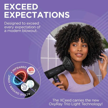 A promotional graphic for the Xceed hair dryer, featuring a woman with voluminous curly hair holding the black hair dryer in a bathroom setting. The background is a solid purple with promotional text and circular product feature callouts highlighting ionic, infrared, and oxygen technology.