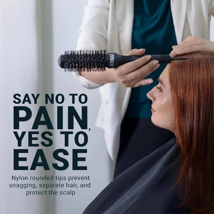 A woman with long red hair sits while a stylist uses a black round hairbrush to separate her hair. Large text on the left reads 'SAY NO TO PAIN, YES TO EASE' with smaller descriptive copy below.