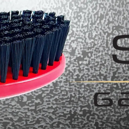 A close-up of a hairbrush with a bright pink-red handle and black bristles, shown against a textured gray background with the text 'SC Gamma+' on the right.