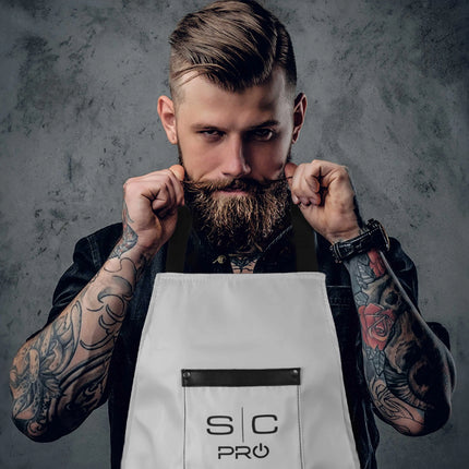 StyleCraft Pro Apron Man with tattoos holding a white apron with 'S C PRO' logo against a gray background