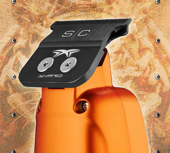 Close-up of an StyleCraft Saber Professional Hair Trimmer – Limited Edition Orange engraved 'S/C' and 'X-PRO' branding, set against a textured metallic background.