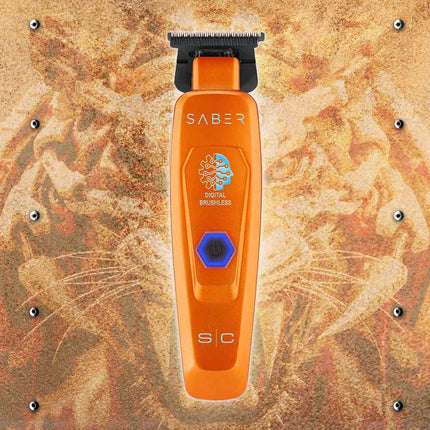 An orange StyleCraft Saber Professional Hair Trimmer – Limited Edition Orange with a black guard head and a blue digital brushless button, centered on a textured brown and gold background with cat whiskers.