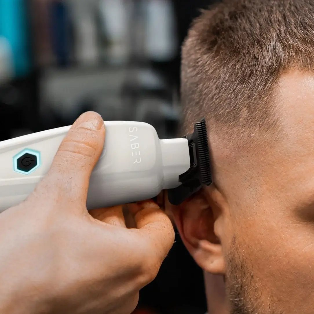 Person using a hair trimmer on their ear with a blurred background