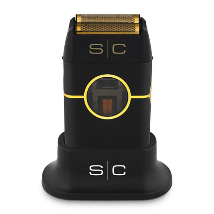 A black and gold Instinct Metal Shaver with a visible brand logo on the front, housed in a charging stand with a clear protective cap on top.