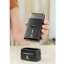 Andis ProFoil Plus II  electric shaver held by a person with a charging station in the foreground.