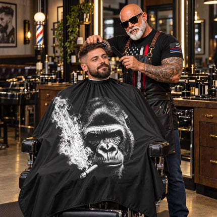 buybarber.com charachter in a barber chair gets a haircut from a tattooed barber wearing sunglasses and an apron. The barber is wearing a black apron over a black t-shirt with a red, white, and blue American flag graphic.