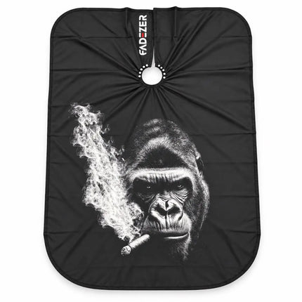 A black salon cape with a graphic print of a gorilla smoking a cigar, featuring a white hanging loop at the top with the brand name 'FAD-ZER' printed vertically.
