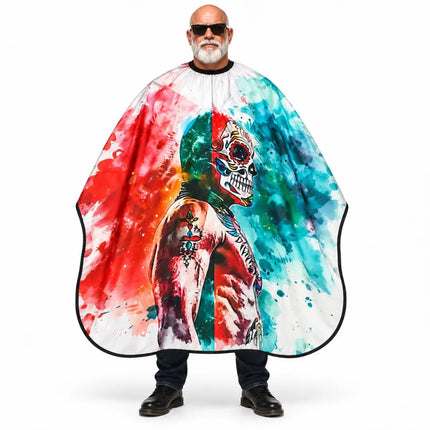 A man wearing a large barber cape with a colorful watercolor-style print featuring a skull and vibrant red, blue, green, and orange splashes on a white background.