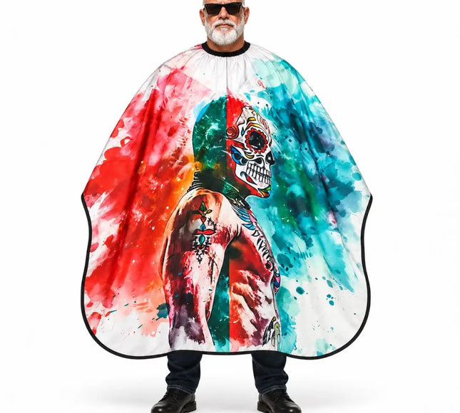 A man wearing a large barber cape with a colorful watercolor-style print featuring a skull and vibrant red, blue, green, and orange splashes on a white background.